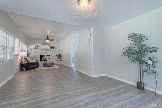 living room with a ceiling fan, wood finished floors, a fireplace, a textured ceiling, and baseboards