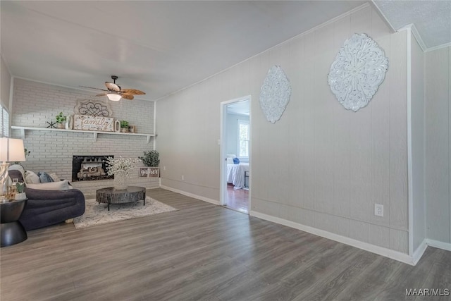 living room featuring a ceiling fan, wood finished floors, ornamental molding, a fireplace, and baseboards