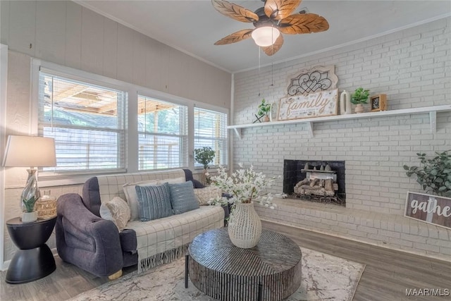 living area with ornamental molding, a ceiling fan, wood finished floors, a fireplace, and brick wall