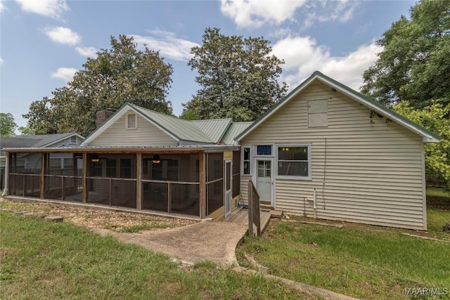 rear view of property with a sunroom, a chimney, and a lawn