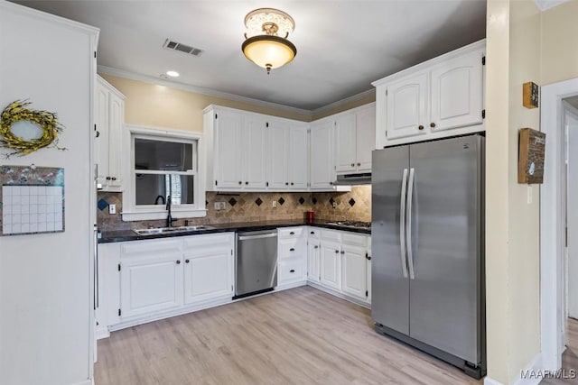 kitchen featuring appliances with stainless steel finishes, a sink, dark countertops, white cabinets, and light wood-type flooring