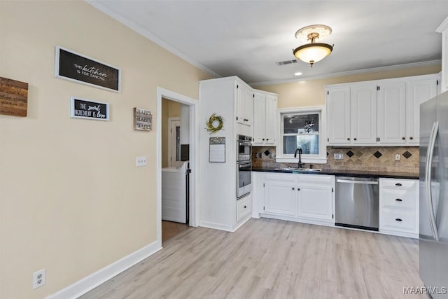 kitchen featuring appliances with stainless steel finishes, a sink, white cabinetry, light wood-style floors, and tasteful backsplash