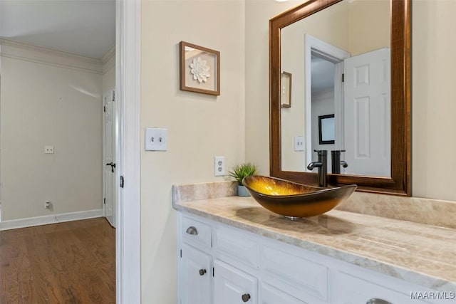 bathroom with wood finished floors, ornamental molding, vanity, and baseboards