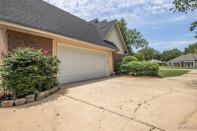view of side of property with brick siding, concrete driveway, roof with shingles, and a garage