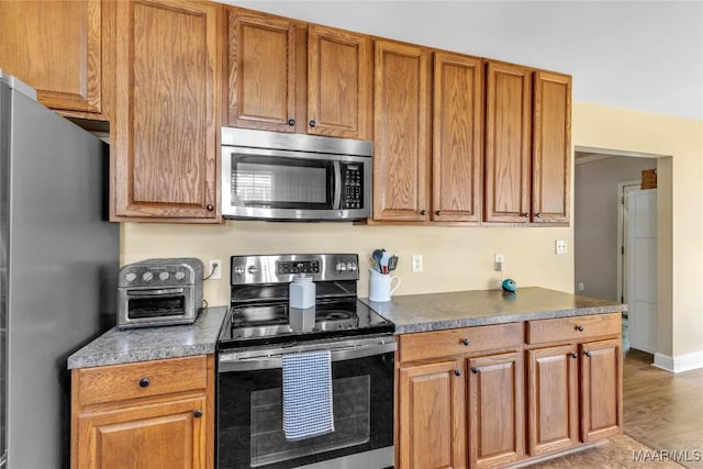 kitchen with appliances with stainless steel finishes, brown cabinetry, dark countertops, and light wood finished floors