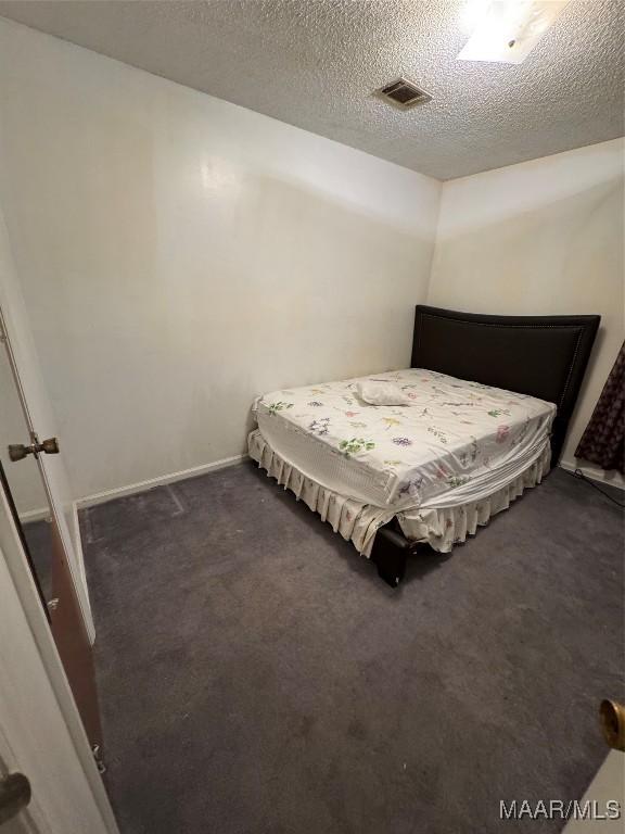 bedroom with dark colored carpet and a textured ceiling