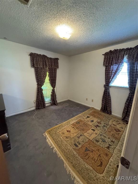 bedroom with a textured ceiling, dark carpet, and baseboards