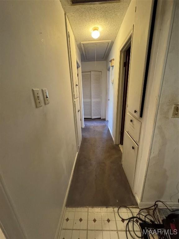 hall featuring attic access, baseboards, carpet flooring, and a textured ceiling