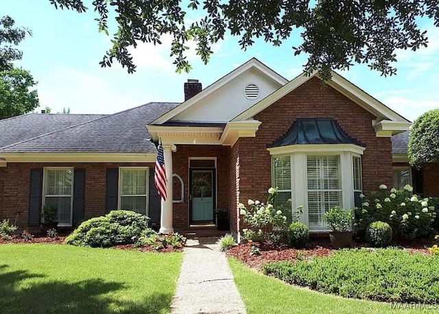 view of front of home featuring brick siding, a front lawn, a chimney, and a shingled roof