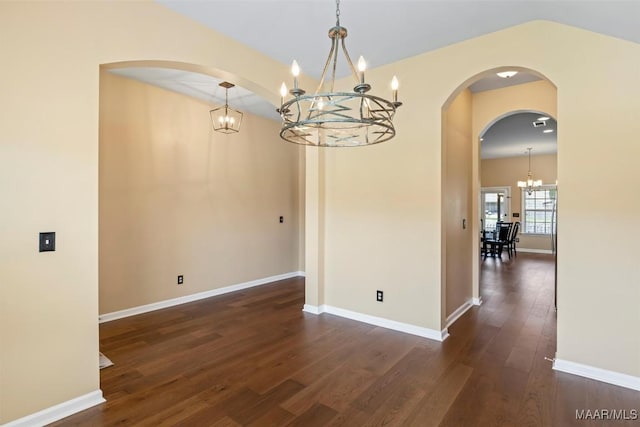 unfurnished dining area featuring a chandelier, dark wood-style floors, baseboards, and arched walkways