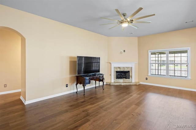 living room with ceiling fan, wood finished floors, arched walkways, a high end fireplace, and baseboards