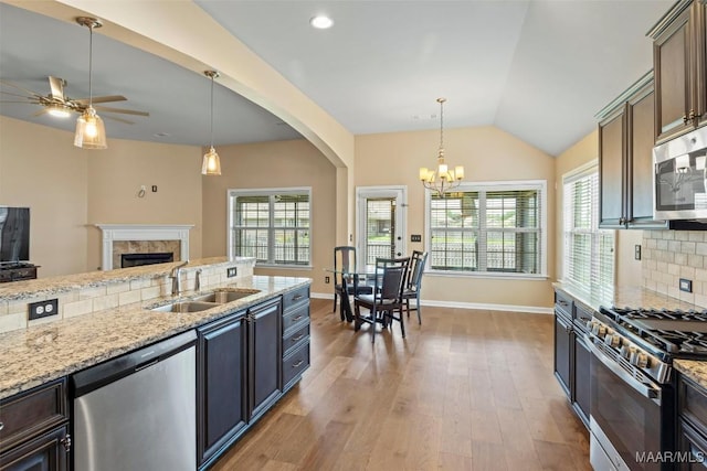 kitchen with stainless steel appliances, a sink, a fireplace, a ceiling fan, and baseboards