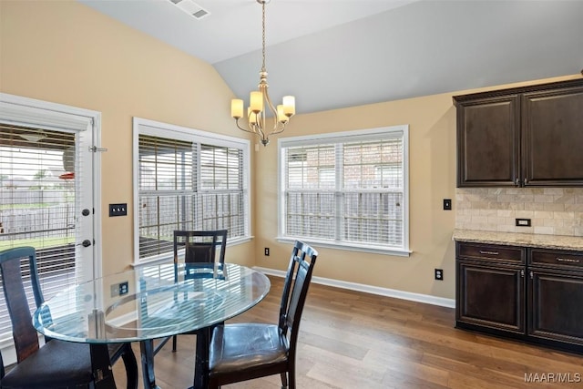 dining area with a chandelier, lofted ceiling, light wood-type flooring, and baseboards