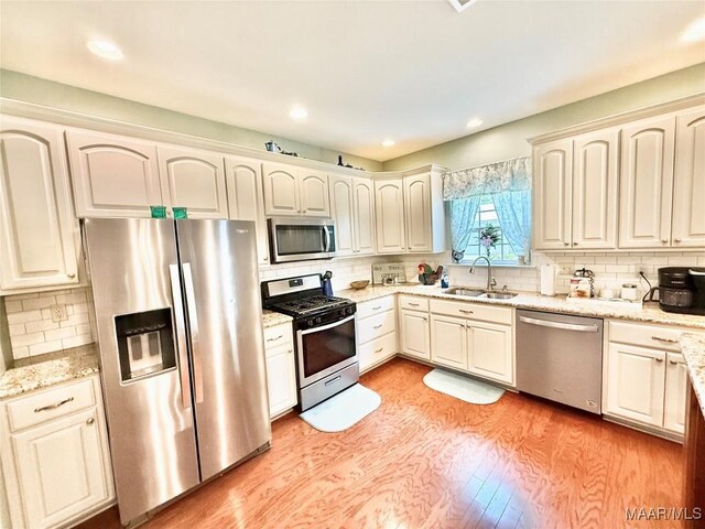 828 Warrior Dr, Valley Grande, AL 36701 - kitchen featuring appliances with stainless steel finishes, a sink, backsplash, light wood-style flooring, and light stone counters