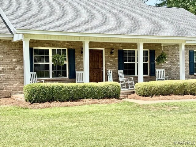 828 Warrior Dr, Valley Grande, AL 36701 - view of exterior entry with a shingled roof, covered porch, brick siding, and a lawn