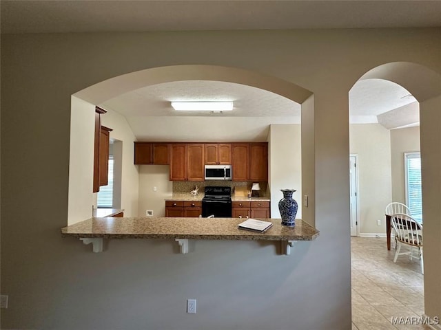 624 Stoneybrooke Way, Montgomery, AL 36117 - kitchen with range, stainless steel microwave, a breakfast bar area, a peninsula, and brown cabinets