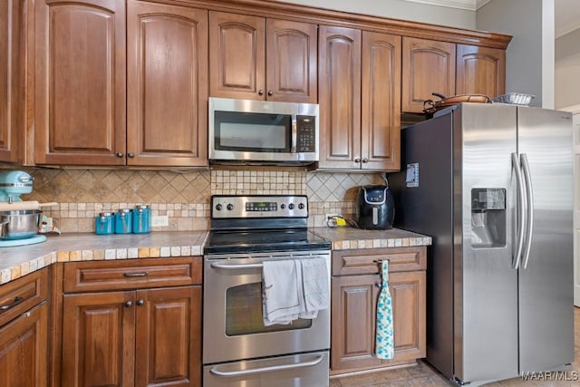 1900 Wyndgate Loop, Montgomery, AL 36117 - kitchen featuring stainless steel appliances, brown cabinets, backsplash, ornamental molding, and tile counters