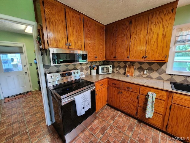445 W Hickory Grove Rd, Lapine, AL 36046 - kitchen featuring appliances with stainless steel finishes, tile countertops, backsplash, and brown cabinetry