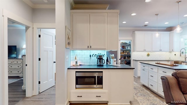 3063 Little Rd, Tallassee, AL 36078 - kitchen with stainless steel microwave, crown molding, dark countertops, light wood-style floors, and white cabinetry