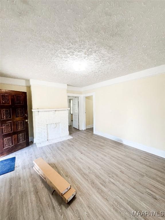 1422 S Holt St, Montgomery, AL 36108 - unfurnished living room with wood finished floors, a textured ceiling, baseboards, and a brick fireplace