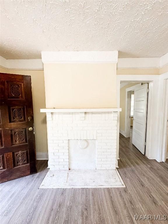 1422 S Holt St, Montgomery, AL 36108 - unfurnished living room with a textured ceiling, wood finished floors, baseboards, and a brick fireplace