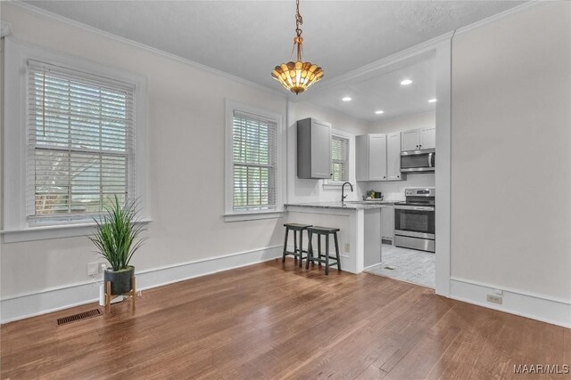 844 E Edgemont Ave, Montgomery, AL 36111 - kitchen featuring appliances with stainless steel finishes, wood finished floors, a kitchen bar, ornamental molding, and hanging light fixtures