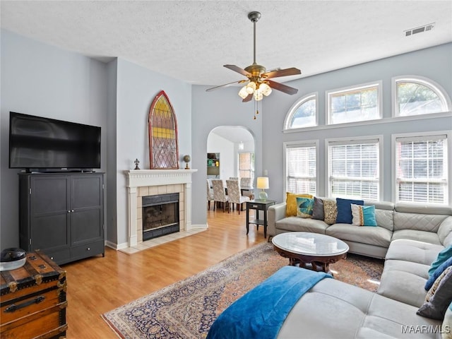 7117 Stamford Ct, Montgomery, AL 36117 - living room with arched walkways, a ceiling fan, light wood-style flooring, a tile fireplace, and a textured ceiling