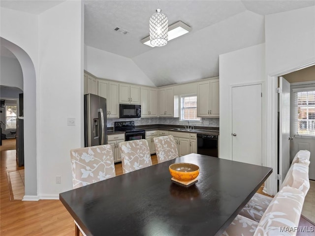 7117 Stamford Ct, Montgomery, AL 36117 - kitchen featuring black appliances, cream cabinets, arched walkways, lofted ceiling, and light wood finished floors