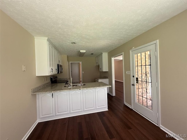 7415 Brampton Ln, Montgomery, AL 36117 - kitchen featuring stainless steel microwave, a peninsula, dark wood-style flooring, white cabinetry, and a textured ceiling
