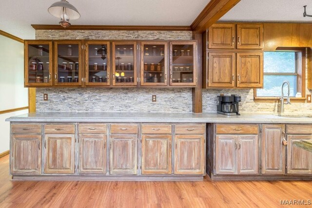 1352 Gibson Rd, Greenville, AL 36037 - kitchen with ornamental molding, glass insert cabinets, tasteful backsplash, light wood-style floors, and brown cabinets