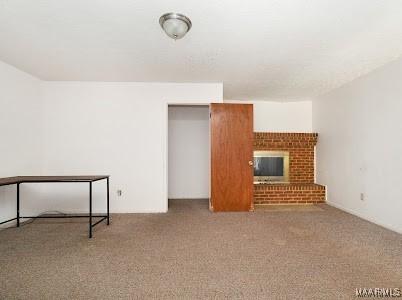 1219 First Ave, Tuskegee, AL 36088 - unfurnished living room featuring carpet and a brick fireplace