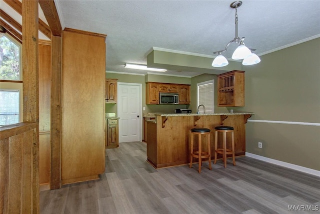 1245 Providence Rd, Titus, AL 36080 - kitchen with stainless steel microwave, light wood-type flooring, a peninsula, a kitchen breakfast bar, and brown cabinets