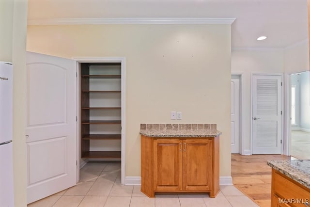 2196 N Ann Ave, Tallassee, AL 36078 - kitchen featuring crown molding, brown cabinets, light stone countertops, light tile patterned floors, and freestanding refrigerator