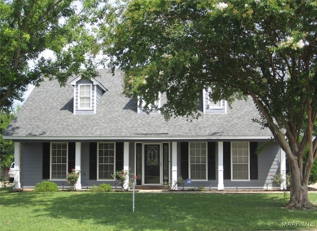 new england style home with a front yard, a porch, and roof with shingles