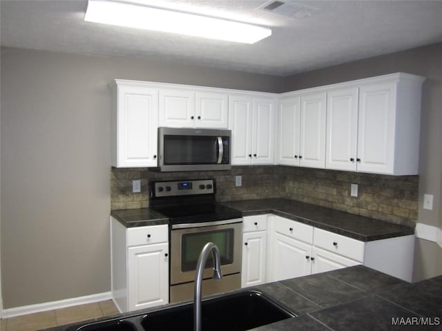 kitchen with stainless steel appliances, dark countertops, decorative backsplash, and white cabinetry