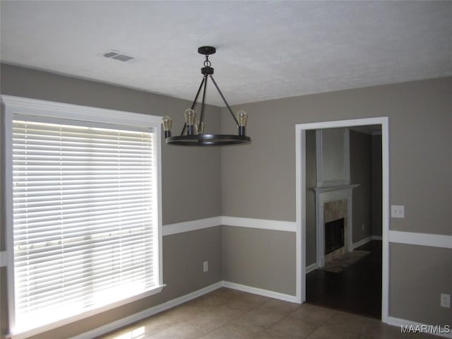 unfurnished dining area featuring a chandelier, tile patterned flooring, and a tile fireplace