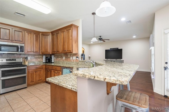 3915 Eagle Ridge Ln, Opelika, AL 36801 - kitchen with stainless steel appliances, a peninsula, a ceiling fan, decorative backsplash, and brown cabinetry