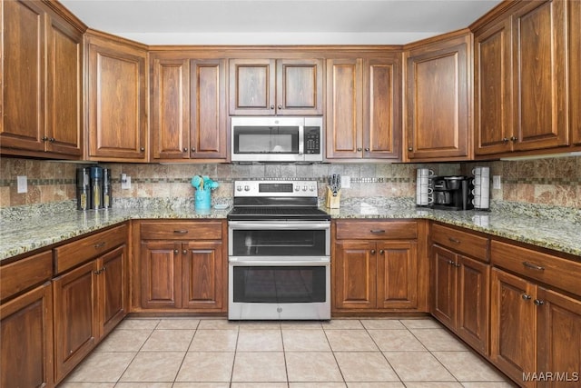 3915 Eagle Ridge Ln, Opelika, AL 36801 - kitchen with appliances with stainless steel finishes, tasteful backsplash, brown cabinetry, and light tile patterned floors