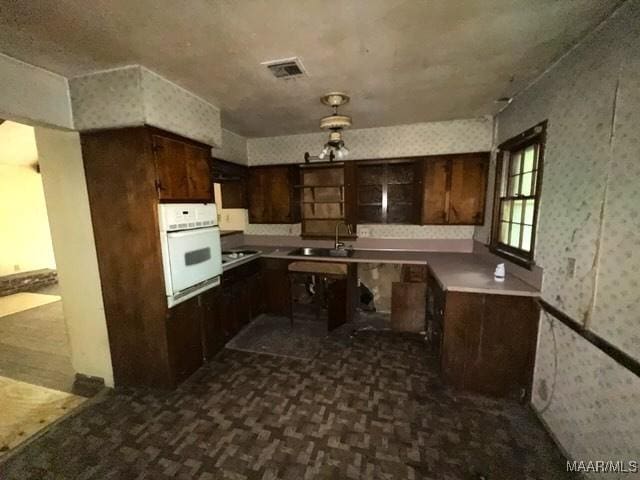 2711 Gwynnbrook Rd, Montgomery, AL 36116 - kitchen featuring white oven, wallpapered walls, dark brown cabinetry, and dark carpet