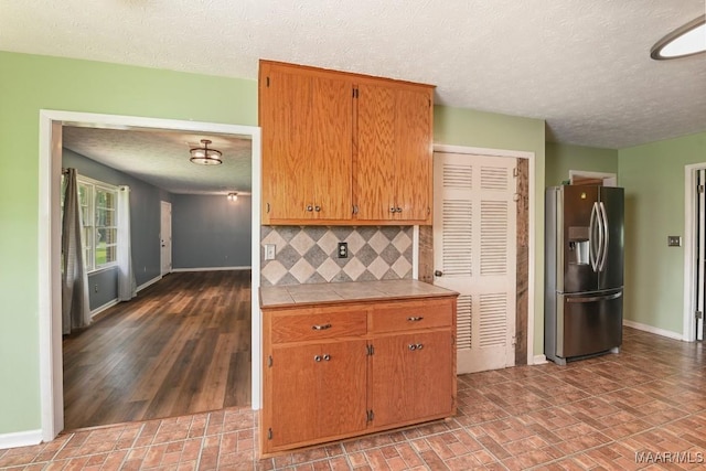 445 W Hickory Grove Rd, Lapine, AL 36046 - kitchen with stainless steel refrigerator with ice dispenser, tile counters, a textured ceiling, tasteful backsplash, and brown cabinets