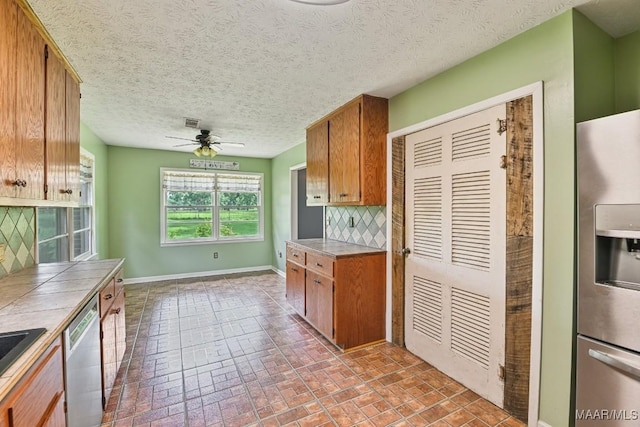 445 W Hickory Grove Rd, Lapine, AL 36046 - kitchen with stainless steel appliances, tile counters, backsplash, brown cabinets, and ceiling fan