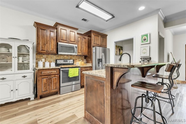 447 Galloway Dr, Wetumpka, AL 36093 - kitchen featuring appliances with stainless steel finishes, ornamental molding, a kitchen breakfast bar, light wood-type flooring, and light stone counters
