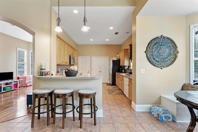 8531 Pipit Ct, Montgomery, AL 36117 - kitchen with stainless steel microwave, light brown cabinets, arched walkways, a peninsula, and a kitchen bar