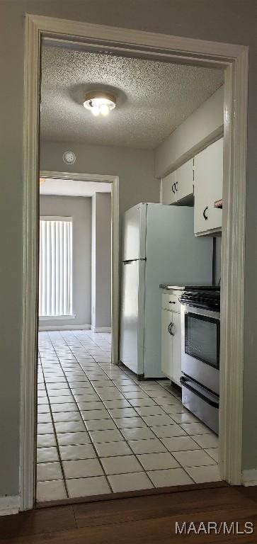 3152 Gentilly Ct, Montgomery, AL 36116 - kitchen with stainless steel range oven, light tile patterned floors, white cabinets, a textured ceiling, and freestanding refrigerator