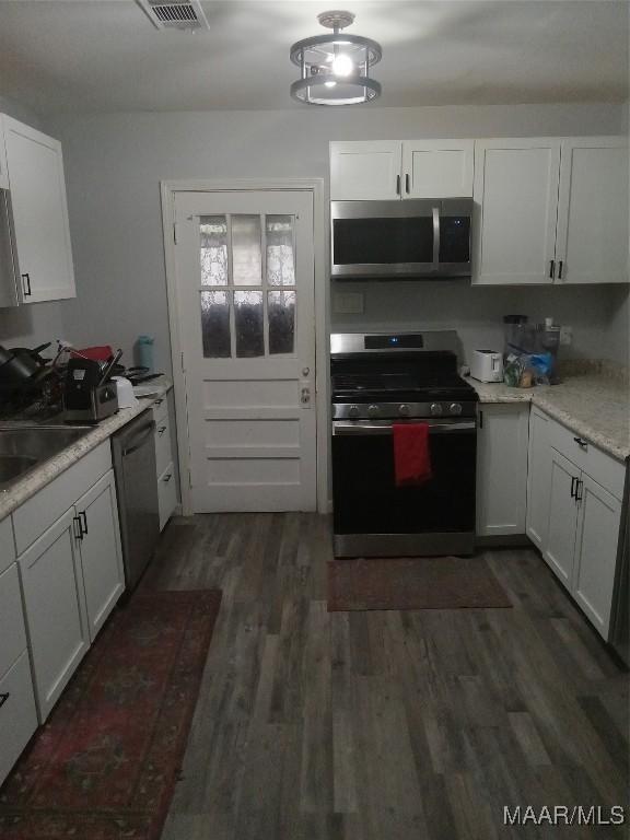 304 Patterson St, Tuskegee, AL 36088 - kitchen with appliances with stainless steel finishes, dark wood-style flooring, white cabinets, and light countertops