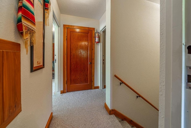 hall with a textured ceiling and light colored carpet