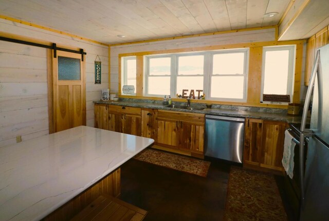 kitchen featuring stainless steel dishwasher, wood walls, a barn door, stone counters, and sink