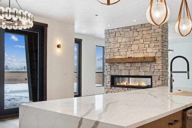 kitchen featuring sink, light stone countertops, a fireplace, and hanging light fixtures