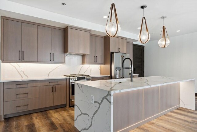 kitchen featuring light stone counters, pendant lighting, stainless steel appliances, hardwood / wood-style floors, and decorative backsplash