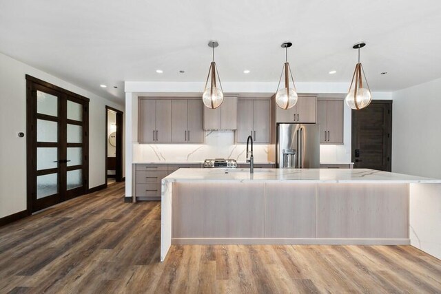 kitchen featuring decorative light fixtures, light stone counters, a spacious island, stainless steel fridge, and dark wood-type flooring